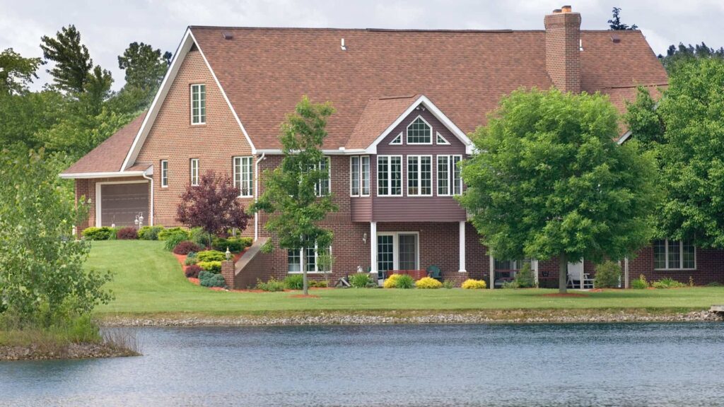 Dom Z Ogrodem Pokrytym Trawnikiem I Drzewami, Otoczony Jeziorem Pod Zachmurzonym Niebem